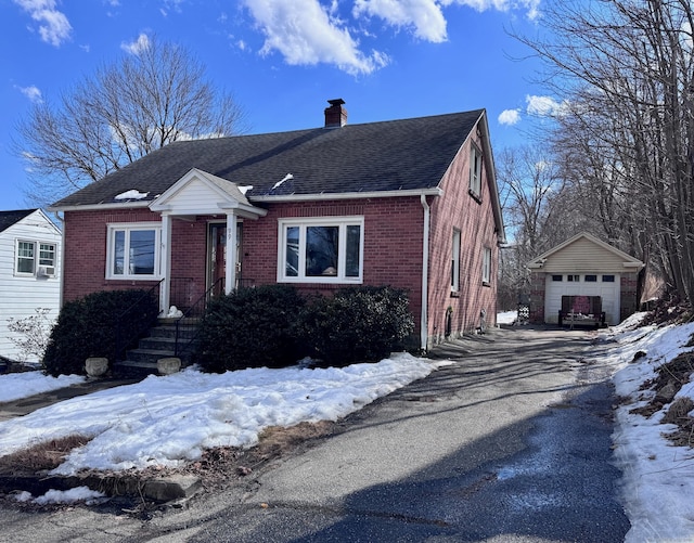 bungalow-style home featuring driveway, brick siding, an outdoor structure, and a chimney