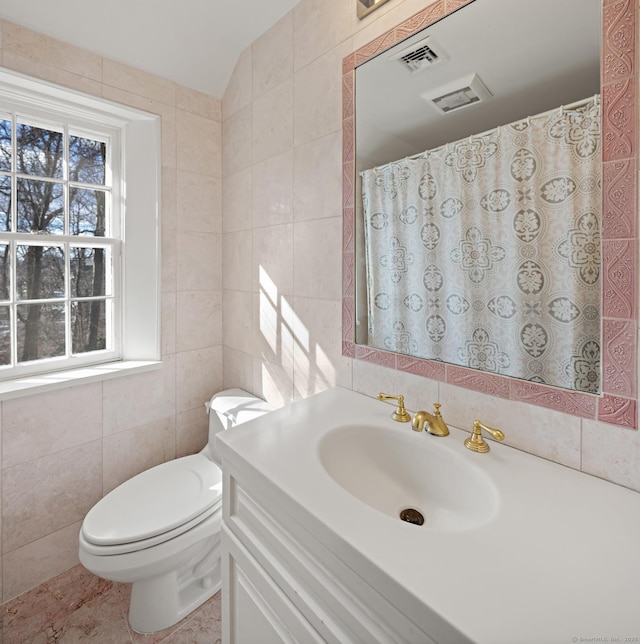 bathroom featuring toilet, visible vents, vanity, and tile walls