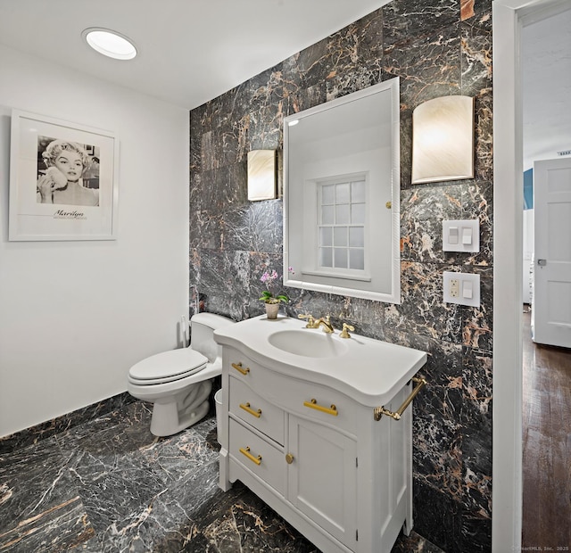 half bath featuring toilet, marble finish floor, tile walls, and vanity