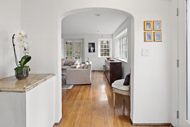 hallway featuring arched walkways and light wood-style flooring