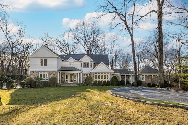 shingle-style home featuring stone siding, a chimney, aphalt driveway, and a front yard