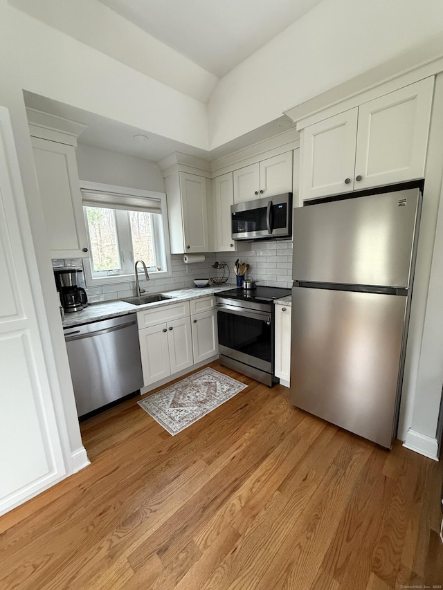 kitchen featuring appliances with stainless steel finishes, white cabinets, a sink, and light wood finished floors