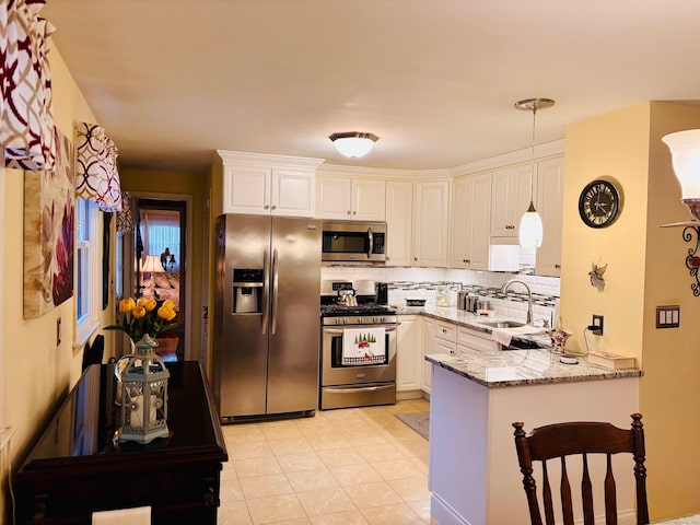 kitchen featuring light stone counters, stainless steel appliances, tasteful backsplash, white cabinets, and a peninsula