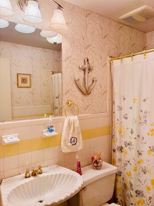 bathroom featuring wallpapered walls, visible vents, a sink, and a wainscoted wall