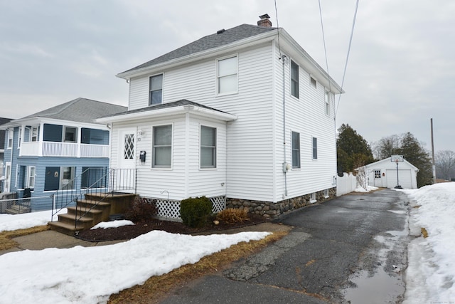 american foursquare style home with aphalt driveway, a chimney, a detached garage, and a shingled roof