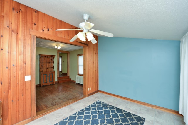 empty room featuring wooden walls, baseboards, a ceiling fan, radiator heating unit, and a textured ceiling