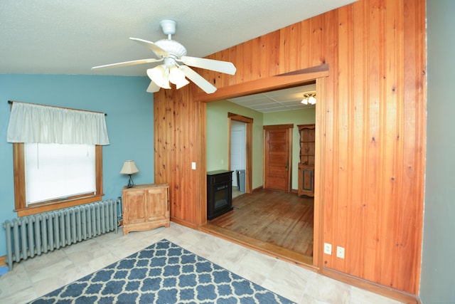 spare room featuring a wood stove, wood walls, a ceiling fan, and radiator