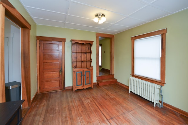 spare room with stairway, radiator, wood-type flooring, and baseboards