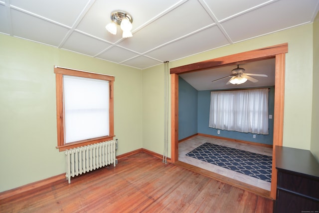 empty room with radiator, a ceiling fan, baseboards, and wood finished floors