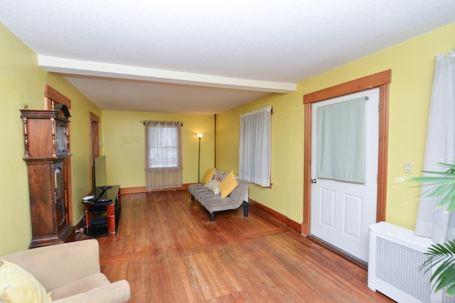 living area with radiator heating unit, a textured ceiling, baseboards, and wood finished floors