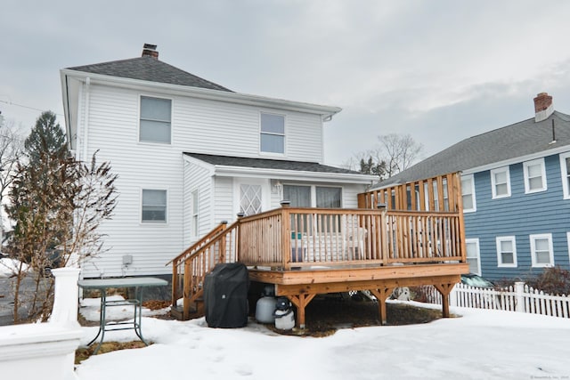 snow covered rear of property featuring a shingled roof, fence, a chimney, and a wooden deck