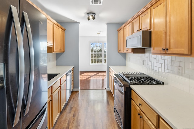 kitchen featuring baseboards, wood finished floors, stainless steel appliances, light countertops, and backsplash