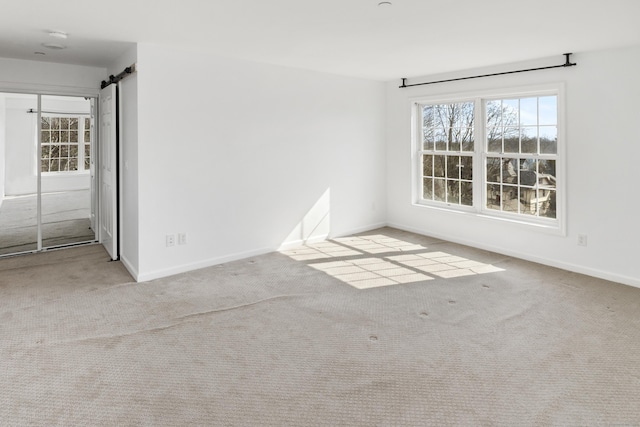 unfurnished room featuring a barn door, carpet, and baseboards