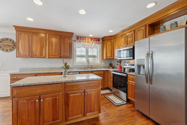 kitchen featuring appliances with stainless steel finishes, a sink, light stone counters, and brown cabinets