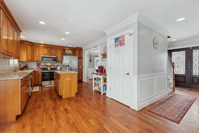 kitchen featuring stainless steel appliances, wood finished floors, a sink, a center island, and light stone countertops