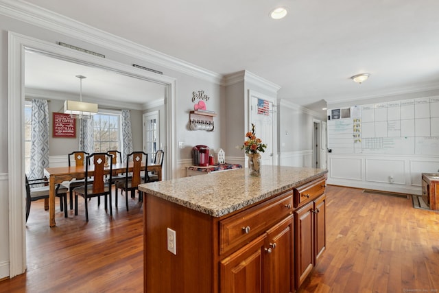 kitchen featuring brown cabinetry, wainscoting, ornamental molding, hardwood / wood-style floors, and light stone countertops