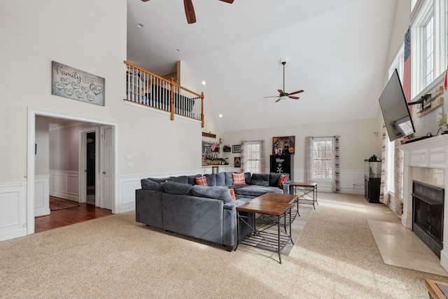 carpeted living room with a high ceiling, wainscoting, a fireplace with flush hearth, and a ceiling fan