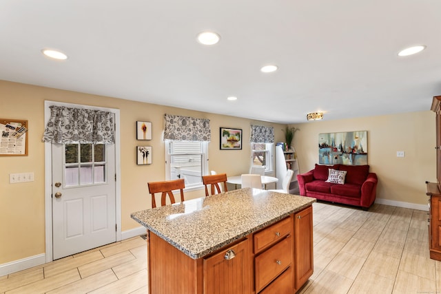 kitchen with baseboards, recessed lighting, a kitchen island, and light stone countertops