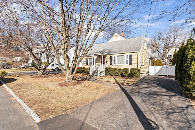 view of front of home featuring aphalt driveway, fence, roof with shingles, a gate, and a chimney