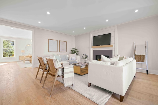 living room with a large fireplace, ornamental molding, light wood finished floors, and recessed lighting