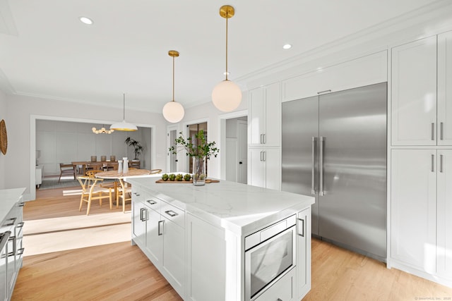 kitchen with light wood finished floors, built in appliances, light stone countertops, crown molding, and white cabinetry