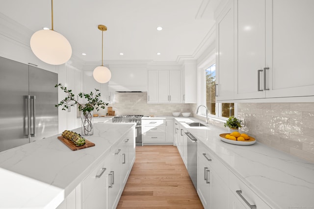 kitchen with high end appliances, hanging light fixtures, decorative backsplash, white cabinetry, and a sink