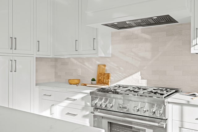 kitchen featuring light stone counters, decorative backsplash, white cabinets, premium range hood, and high end range