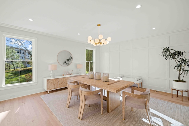 dining space with light wood-type flooring, a chandelier, a decorative wall, and ornamental molding