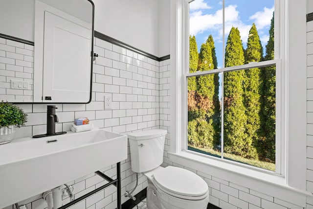 bathroom with a sink, toilet, and tile walls