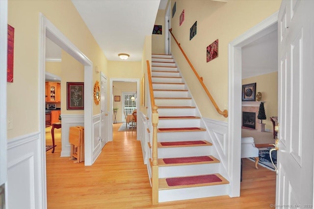 stairway with a fireplace, wainscoting, wood finished floors, and a decorative wall