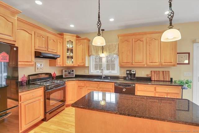 kitchen featuring under cabinet range hood, a sink, light wood-type flooring, black appliances, and dark stone countertops