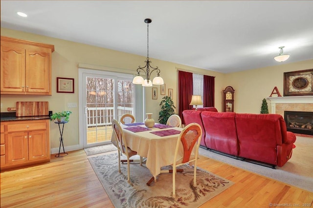 dining room featuring light wood finished floors, baseboards, an inviting chandelier, and a glass covered fireplace