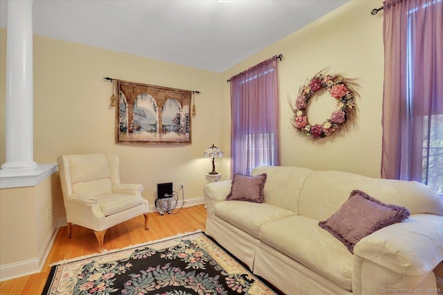 living area with baseboards, wood finished floors, and ornate columns