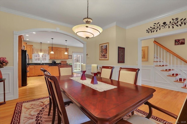 dining area featuring arched walkways, stairs, ornamental molding, wainscoting, and light wood finished floors