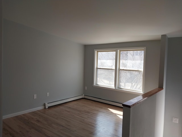 empty room with a baseboard heating unit, baseboards, and wood finished floors