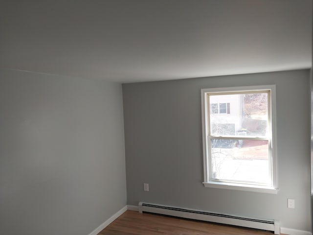 unfurnished room featuring baseboards, a baseboard heating unit, and wood finished floors