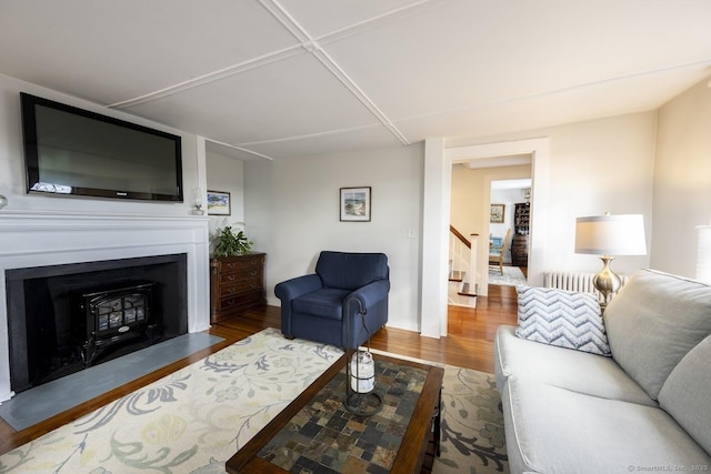 living area featuring a fireplace with flush hearth, radiator, stairway, and wood finished floors