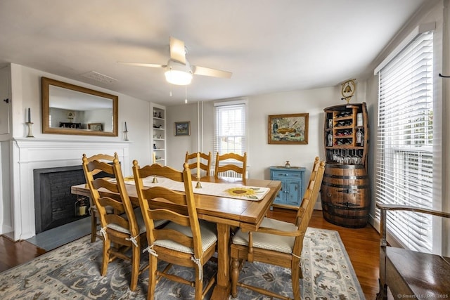 dining area featuring ceiling fan, a fireplace, built in shelves, and wood finished floors