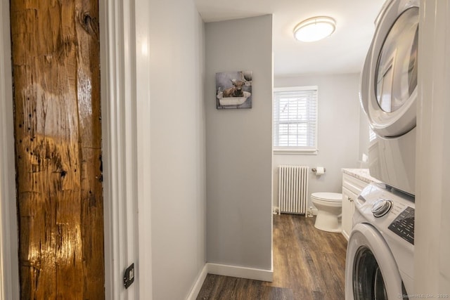 bathroom with stacked washer and dryer, toilet, radiator heating unit, wood finished floors, and baseboards