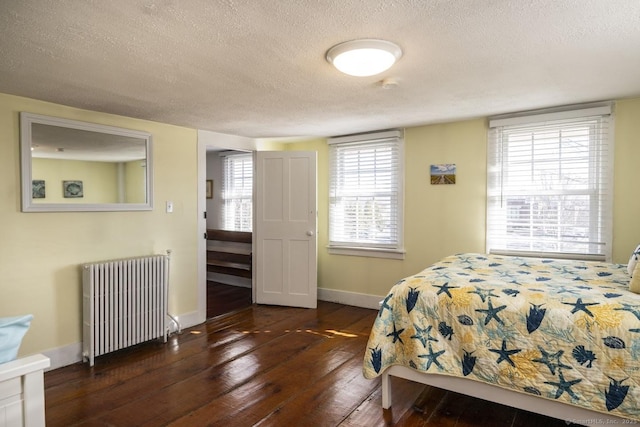 bedroom featuring a textured ceiling, radiator heating unit, dark wood finished floors, and baseboards