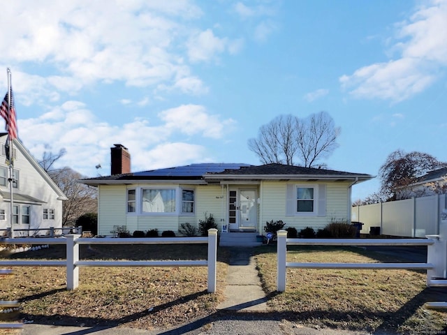 single story home with a chimney, fence, and roof mounted solar panels