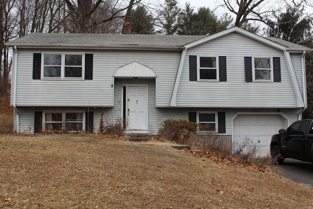 raised ranch featuring an attached garage, driveway, and a chimney