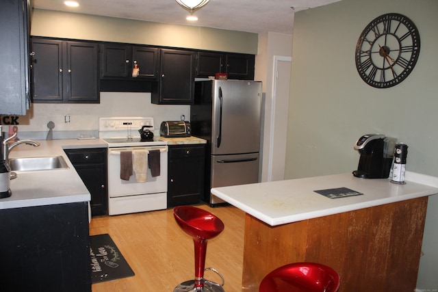 kitchen featuring white range with electric cooktop, light countertops, freestanding refrigerator, a sink, and dark cabinets