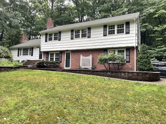 view of front facade with brick siding, a chimney, and a front lawn