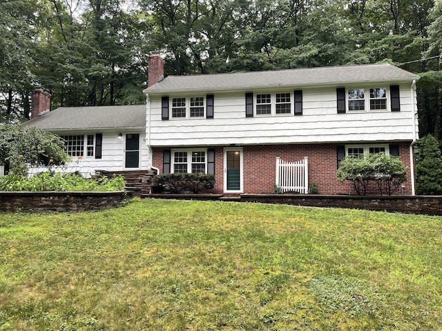 tri-level home with brick siding, a chimney, and a front lawn