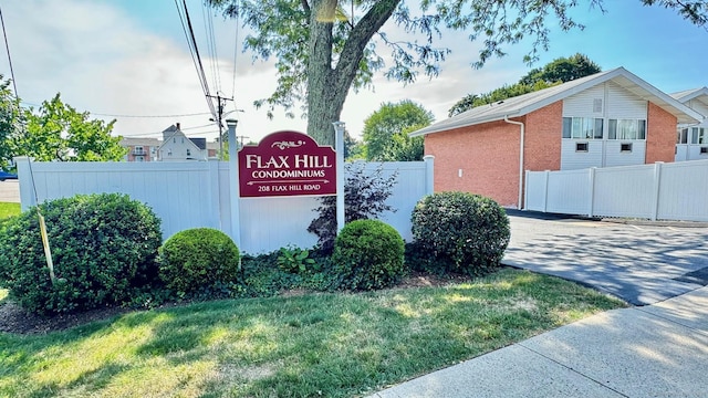 community / neighborhood sign featuring fence and a lawn