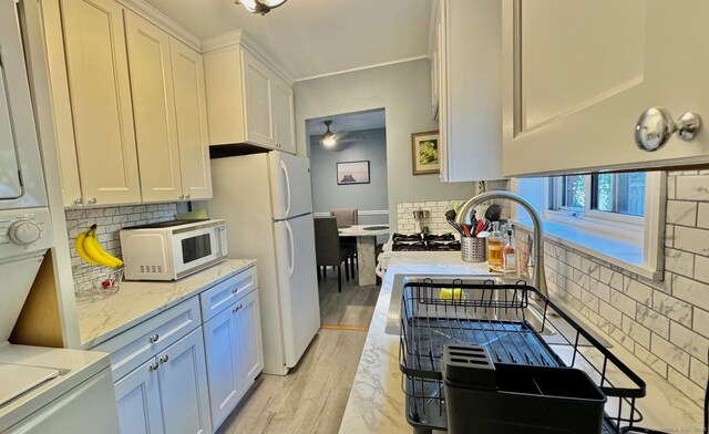 kitchen featuring stacked washer and dryer, light wood-style flooring, backsplash, white cabinets, and white appliances