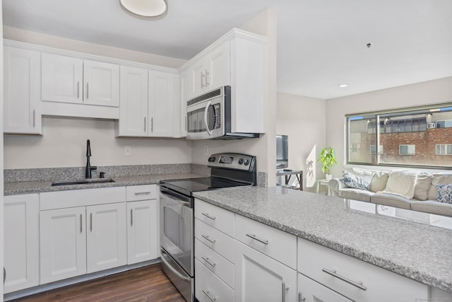 kitchen with light stone counters, a sink, white cabinets, appliances with stainless steel finishes, and dark wood finished floors