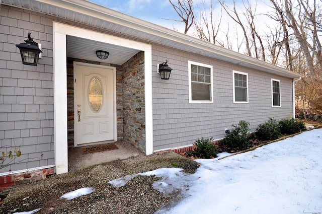 snow covered property entrance with stone siding