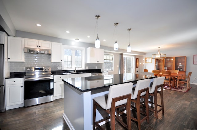 kitchen featuring under cabinet range hood, a sink, stainless steel electric range, dark countertops, and dark wood finished floors